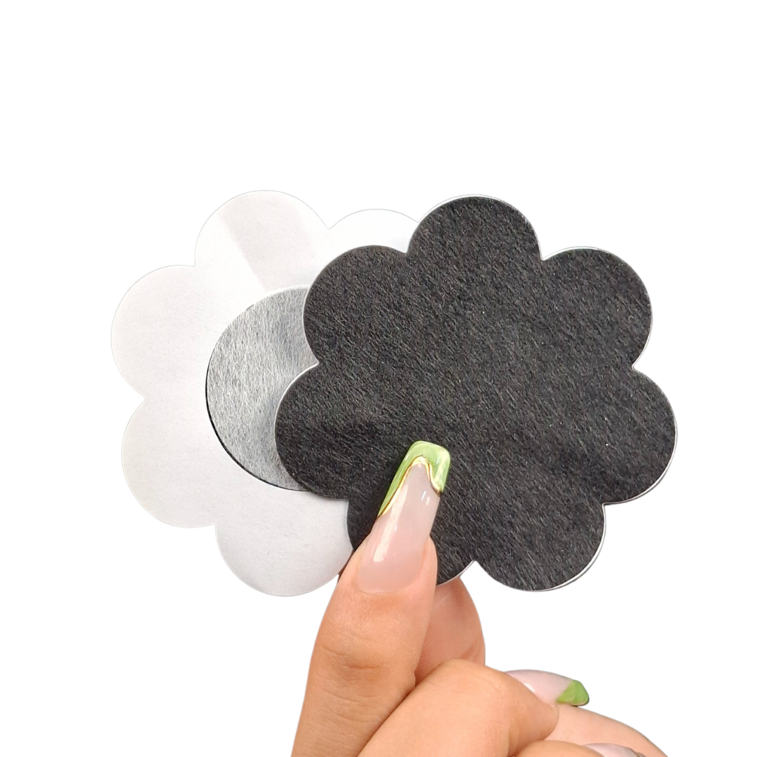 Manos sosteniendo dos tapa pezones adhesivos en forma de corazón, uno blanco y uno rosa, diseñados para cubrir los pezones de forma discreta bajo la ropa.